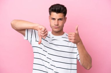 Pembe arka planda izole edilmiş beyaz bir adam iyiye-kötüye işaret yapıyor. Evet ya da hayır arasında kararsız