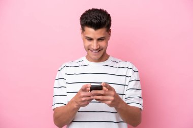 Pembe arka planda izole edilmiş genç beyaz adam cep telefonuyla bir mesaj gönderiyor.