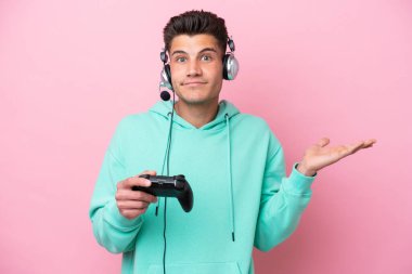 Pembe arka planda izole edilmiş bir bilgisayar oyunu kontrolörüyle oynayan yakışıklı beyaz adam ellerini kaldırırken şüpheye düşüyor.