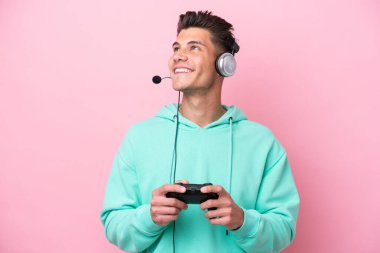 Pembe arka planda izole edilmiş bir bilgisayar oyunu kontrolörüyle oynayan yakışıklı beyaz bir adam yukarı bakarken bir fikir düşünüyor.