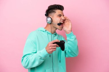 Pembe arka planda izole edilmiş bir bilgisayar oyunu kontrolörüyle oynayan yakışıklı beyaz bir adam ağzı sonuna kadar açık bağırıyor.