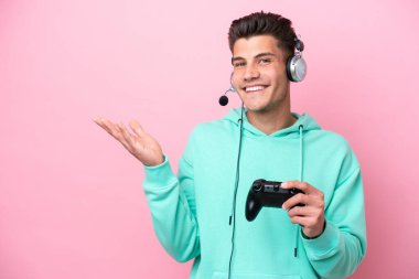 Pembe arka planda izole edilmiş bir bilgisayar oyunu kontrolörüyle oynayan yakışıklı beyaz bir adam davet edildiği için ellerini yana uzatıyor.