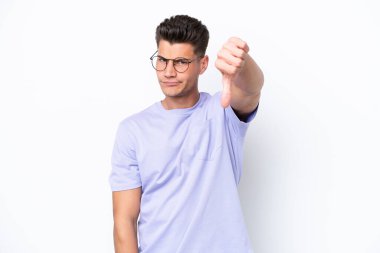 Beyaz arka planda izole genç beyaz adam olumsuz ifade ile baş parmağını göstermektedir