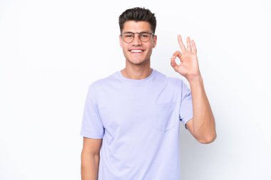 Beyaz arka planda izole edilmiş genç beyaz adam parmaklarıyla tamam işareti gösteriyor.