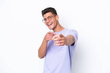 Beyaz arka planda izole edilmiş genç beyaz adam şaşırmış ve ön tarafı işaret ediyor.