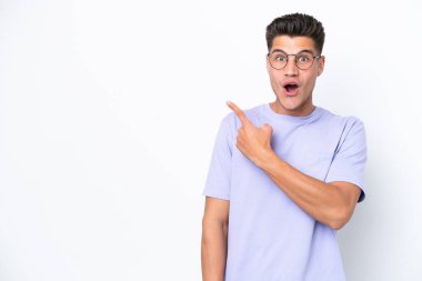 Beyaz arka planda izole edilmiş genç beyaz adam şaşırmış ve işaret ediyor.