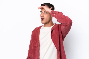 Beyaz arka planda izole edilmiş genç beyaz adam yan tarafa bakarken sürpriz jest yapıyor.