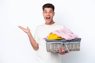 Çamaşır sepetini tutan beyaz arka planda yüzü şoke olmuş genç beyaz bir adam.