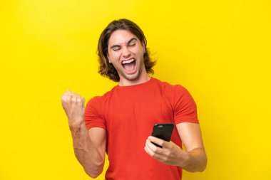 Sarı arka planda izole edilmiş, telefon zafer pozisyonunda beyaz yakışıklı bir adam.