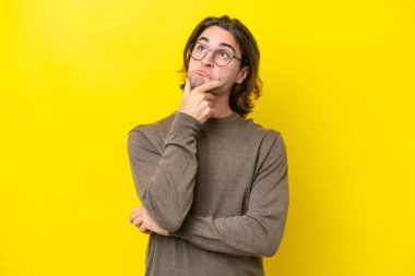 Caucasian handsome man isolated on yellow background having doubts