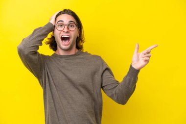 Sarı arka planda izole edilmiş beyaz yakışıklı adam şaşırdı ve parmağını yana çevirdi.