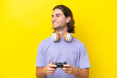 Sarı arka planda izole edilmiş bir bilgisayar oyunu kontrolörüyle oynayan yakışıklı beyaz bir adam.