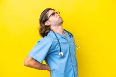 Genç cerrah beyaz adam, sarı arka planda izole edilmiş, gayret gösterdiği için sırt ağrısı çekiyor.