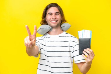 Şişirilebilir seyahat yastığı olan yakışıklı adam gülümsüyor ve zafer işareti gösteriyor.