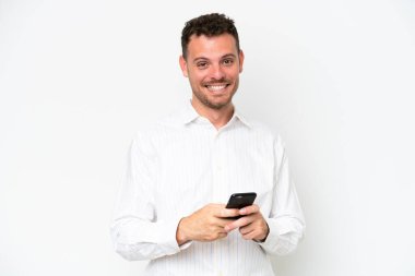 Beyaz arka planda izole edilmiş beyaz saçlı yakışıklı bir adam cep telefonuyla mesaj yolluyor.