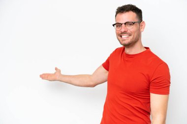 Beyaz arka planda soyutlanmış beyaz tenli yakışıklı adam, davet edilmek için ellerini yana uzatıyor.