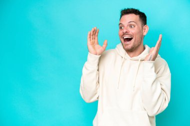 Mavi arka planda yalıtılmış beyaz, yakışıklı, şaşırtıcı bir yüz ifadesi olan genç adam.