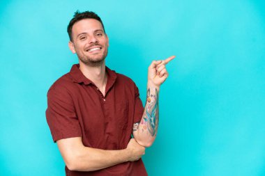 Beyaz tenli yakışıklı adam mavi arka planda izole edilmiş, parmağıyla kenarı gösteriyor.