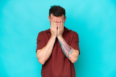 Kafkasyalı yakışıklı genç adam mavi arka planda izole edilmiş, yorgun ve hasta bir ifadeyle.