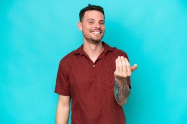 Beyaz tenli yakışıklı bir adam mavi arka planda izole edilmiş ve bizimle gelmesi için davet ediliyor. Gelmene sevindim.