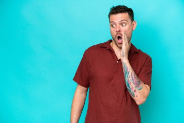 Beyaz tenli yakışıklı adam mavi arka planda izole edilmiş. Yan tarafa bakarken sürpriz bir jest yapıyor.