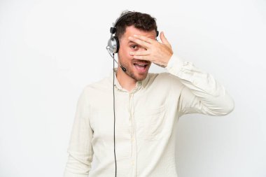 Tele pazarlamacı, beyaz arka planda kulaklıkla çalışan beyaz bir adam. Gözleri elleriyle kaplıyor ve gülümsüyor.