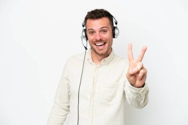 Tele pazarlamacı, beyaz arka planda izole edilmiş kulaklıkla çalışan beyaz bir adam gülümsüyor ve zafer işareti gösteriyor.