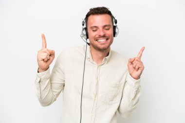 Tele pazarlamacı beyaz arka planda izole edilmiş kulaklıkla çalışan beyaz bir adam parmak uçlarını işaret ediyor ve mutlu.