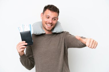 Beyaz arka planda izole edilmiş pasaport taşıyan genç beyaz bir adam baş parmak hareketi yapıyor.