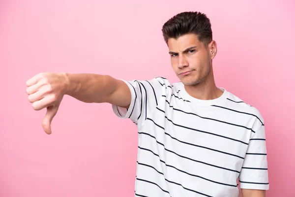 ピンクの背景に孤立した若い白人男性は 否定的な表現で親指を下に示す — ストック写真