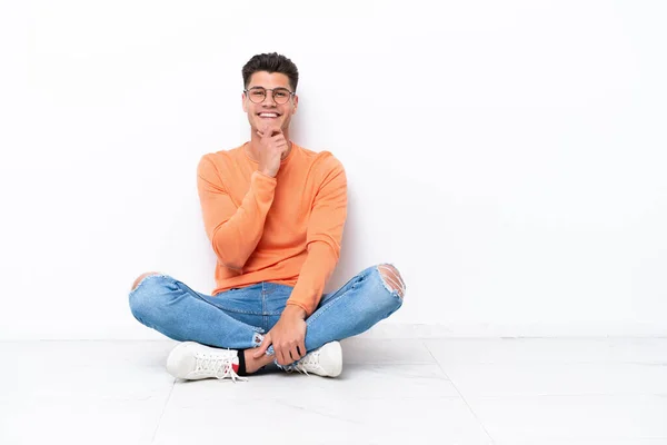 Νεαρός Κάθεται Στο Πάτωμα Απομονωμένος Λευκό Φόντο Γυαλιά Και Χαμογελώντας — Φωτογραφία Αρχείου