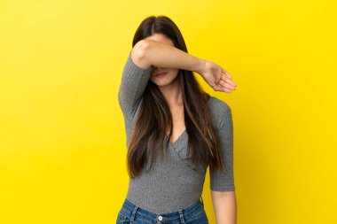 Sarı arka planda izole edilmiş genç Brezilyalı kadın gözlerini elleriyle kapatıyor.