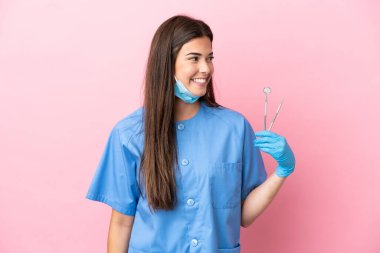 Dişçi kadının elinde pembe arka planda izole edilmiş aletler var.