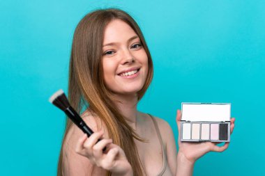 Mavi arka planda, makyajlı ve mutlu genç beyaz kadın.