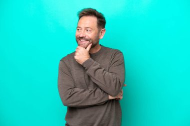 Mavi arka planda soyutlanmış orta yaşlı beyaz bir adam yana bakıyor ve gülümsüyor.