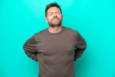 Orta yaşlı, beyaz bir adam mavi arka planda izole edilmiş. Çaba gösterdiği için sırt ağrısı çekiyor.