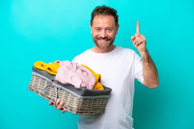 Mavi arka planda izole edilmiş çamaşır sepetini tutan orta yaşlı kadın harika bir fikre işaret ediyor.