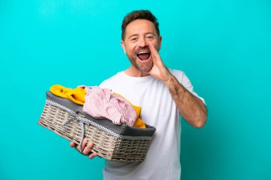 Mavi arka planda izole edilmiş çamaşır sepetini tutan orta yaşlı bir kadın ağzı açık bağırıyor.