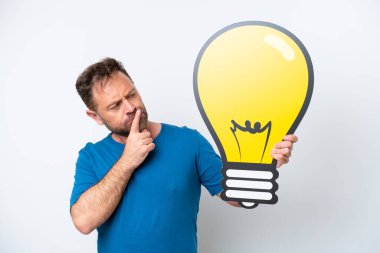 Beyaz arka planda izole edilmiş orta yaşlı beyaz bir adam elinde bir ampul simgesi tutuyor ve şüpheleri var.