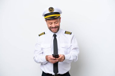 Uçak orta yaş pilotu beyaz arka planda izole edildi ve cep telefonuyla bir mesaj gönderiyor.