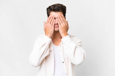 İzole edilmiş beyaz arka planda genç, yakışıklı beyaz bir adam. Gözlerini elleriyle kapatıyor.