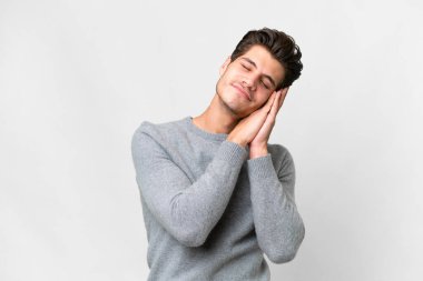 İzole edilmiş beyaz arka planda genç, yakışıklı, beyaz bir adam uyku jesti yapıyor.