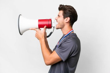 Young caucasian man with medals over isolated white background shouting through a megaphone