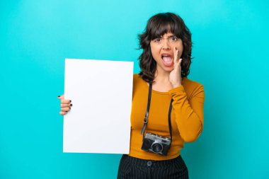 Young photographer latin woman isolated on blue background holding an empty placard and shouting clipart