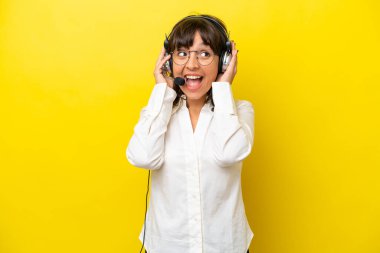 Tele pazarlamacı Latin kadın sarı arka planda izole bir kulaklıkla çalışıyor.