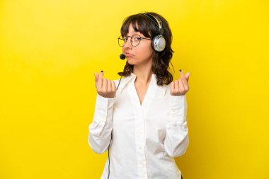 Tele pazarlamacı Latin kadın sarı arka planda izole bir kulaklıkla çalışıyor.