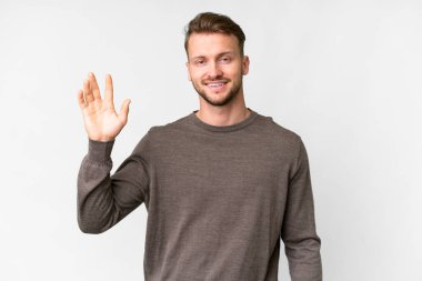 Young handsome caucasian man over isolated white background saluting with hand with happy expression