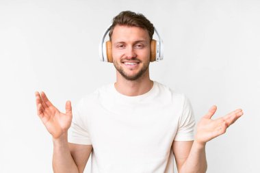 Soyutlanmış beyaz arka plandaki yakışıklı beyaz adam şaşırdı ve müzik dinliyor.