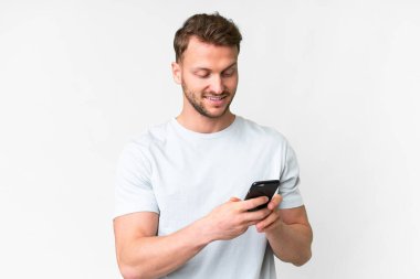 İzole edilmiş beyaz arka planı olan yakışıklı beyaz bir adam cep telefonuyla mesaj ya da e-posta yolluyor.