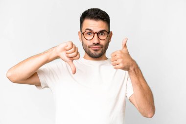 Young handsome caucasian man over isolated white background making good-bad sign. Undecided between yes or not